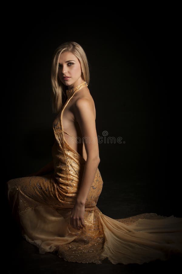 Color image of beautiful blonde woman wearing a revealing golden halterneck evening dress, captured in beautiful dramatic glamor lighting. Color image of beautiful blonde woman wearing a revealing golden halterneck evening dress, captured in beautiful dramatic glamor lighting.