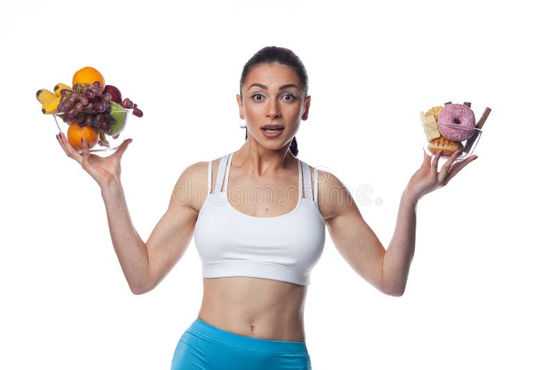 Sexy brunette woman in fitness suit eating fruits and candies