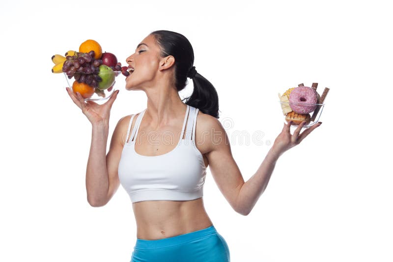 Sexy brunette woman in fitness suit eating fruits and candies