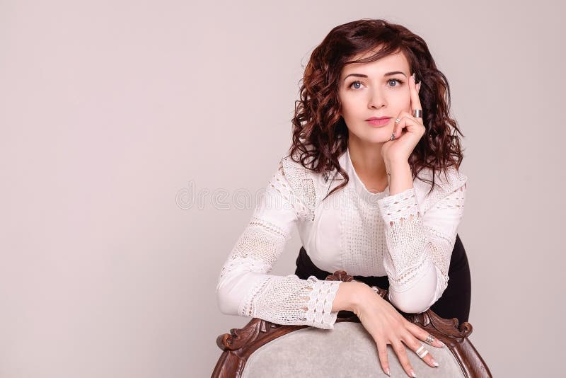 Sexy curly brunette leaned on a beautiful vintage armchair. Business elegant girl, business photo shoot on a light background . stock image Sexy curly brunette leaned on a beautiful vintage armchair. Business elegant girl, business photo shoot on a light background . stock image