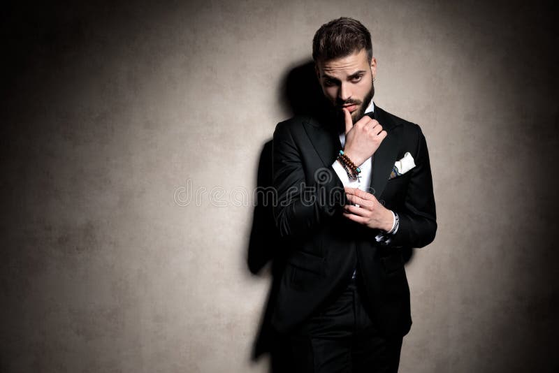 Sexy elegant man in tuxedo touching lips in a fashion pose