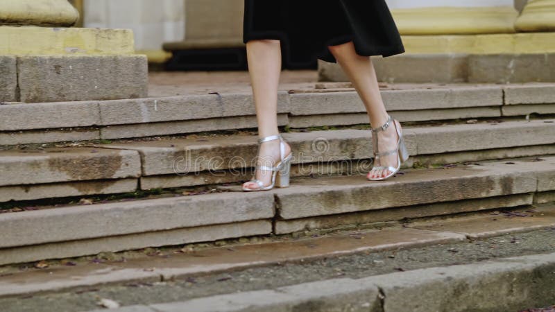 Sexy female legs in silver sandals with heels go along stairs