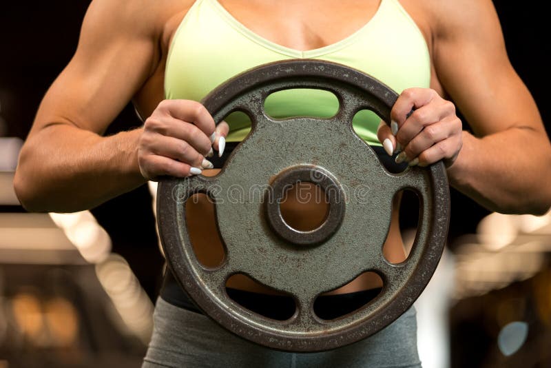 Sexy fitness blonde woman is standing with weight plate in the gym