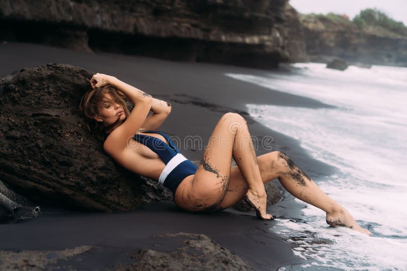 Sexy girl with big breasts in blue swimwear relaxing at beach with black sand. stock photo Sexy girl with big breasts in blue swimwear relaxing at beach with black sand. stock photo