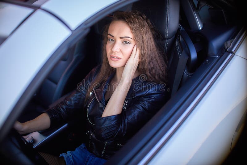 sexy girl in a leather jacket, denim shorts and black pantyhose in the net sits at the wheel of a car.