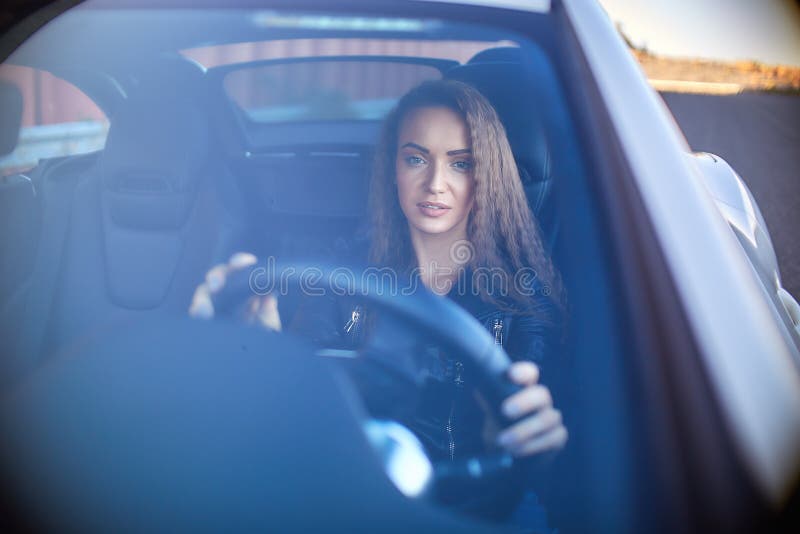 sexy girl in a leather jacket, denim shorts and black pantyhose in the net sits at the wheel of a car.