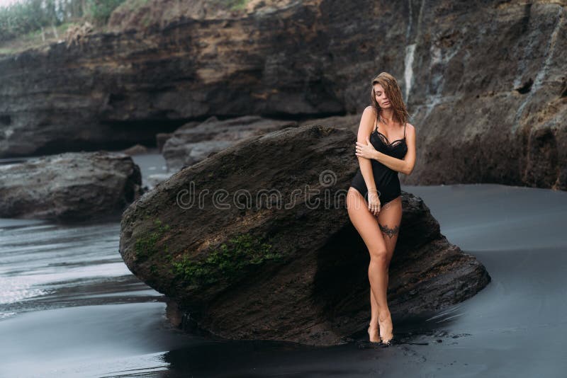 Sexy girl in swimsuit with tattoo on her leg poses near big stone on sandy beach royalty free stock photos Sexy girl in swimsuit with tattoo on her leg poses near big stone on sandy beach royalty free stock photos