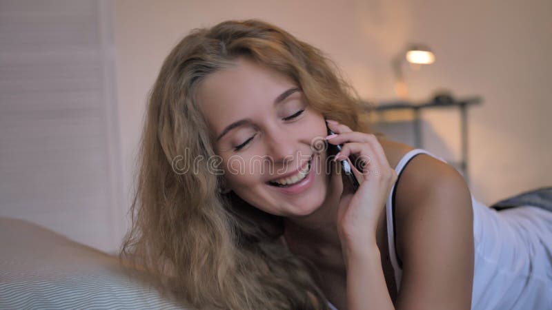 Sexy girl in a white tank top and blue short denim shorts speaks on the phone and laughs