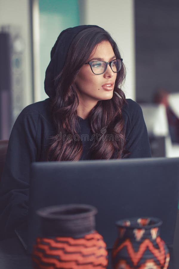 Sexy young Caucasian woman in hoodie looking away while thinking and inspirating at laptop. Sexy young Caucasian woman in hoodie looking away while thinking and inspirating at laptop