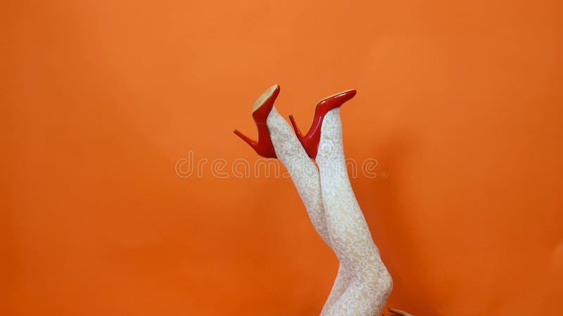 Sexy long legs on high heels red shoes and white fishnet stockings on orange background. Retro style