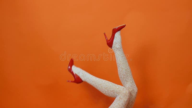 Sexy long legs on high heels red shoes and white fishnet stockings on orange background. Retro style