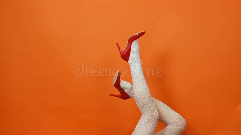 Sexy long legs on high heels red shoes and white fishnet stockings on orange background. Retro style