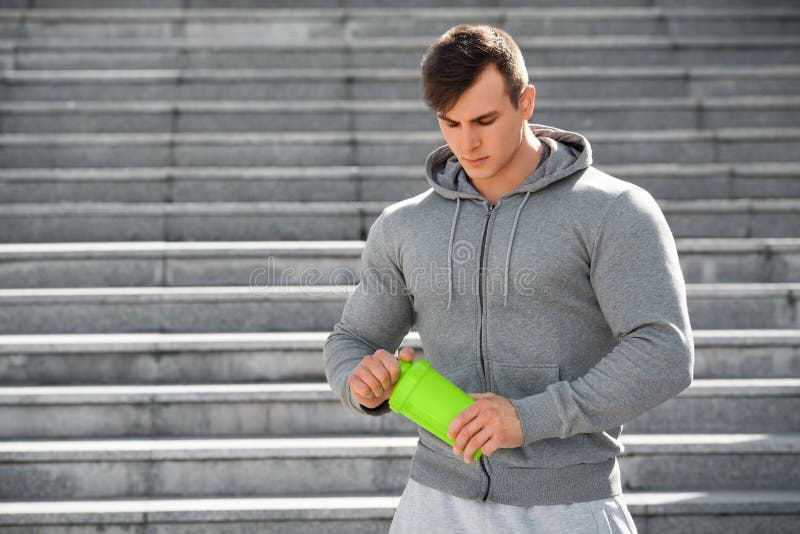muscular man holding shaker, outdoors. Young active male drinking water.