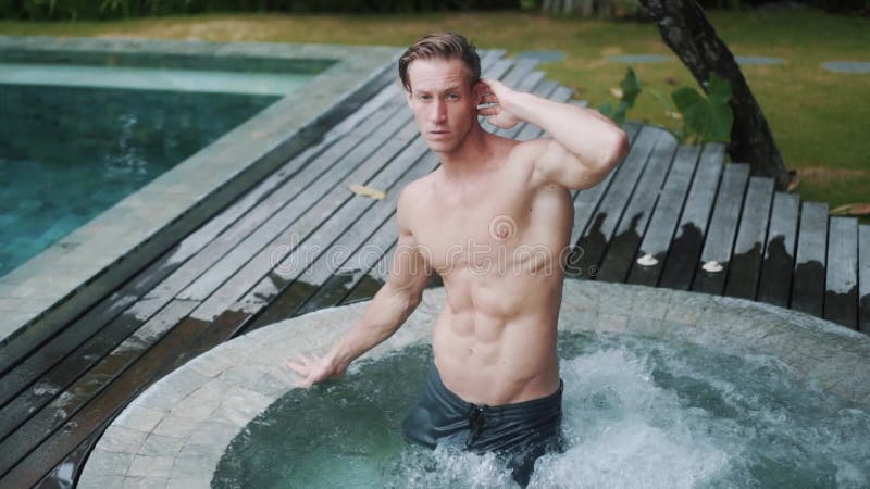 Sexy Männer Modell mit dem sportlichen Körper, der in der Jacuzzibadzeitlupe darstellt