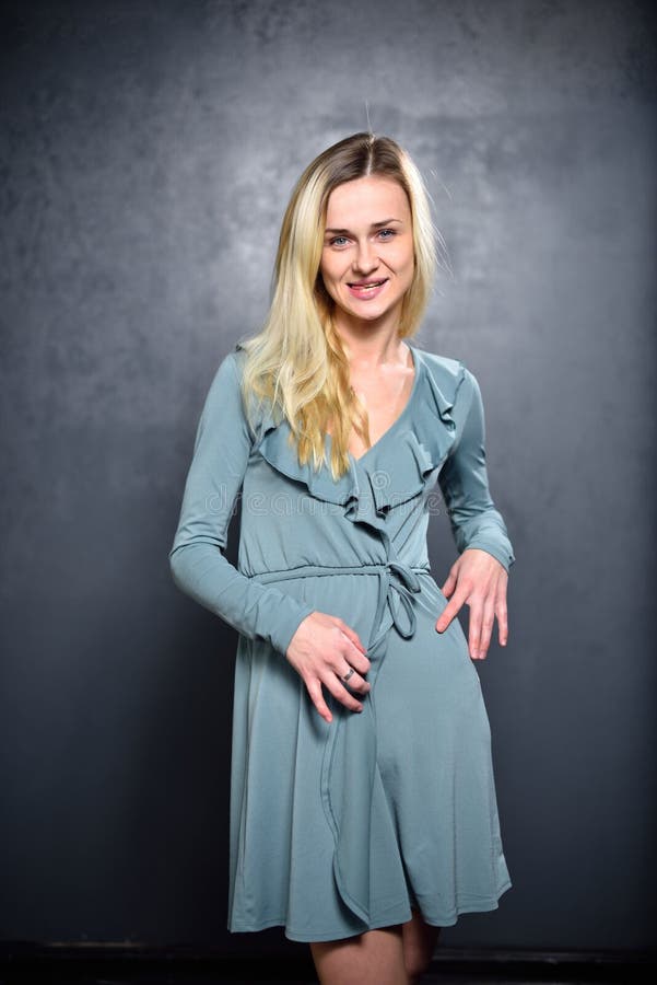 Skinny Blonde Girl In Gray Dress On The Background Of Gray Wall Stock