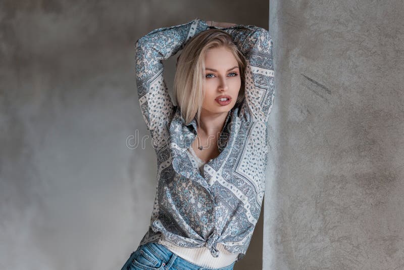 Sexy stylish young blond woman in a fashionable shirt with a pattern in a T-shirt in jeans posing in a studio