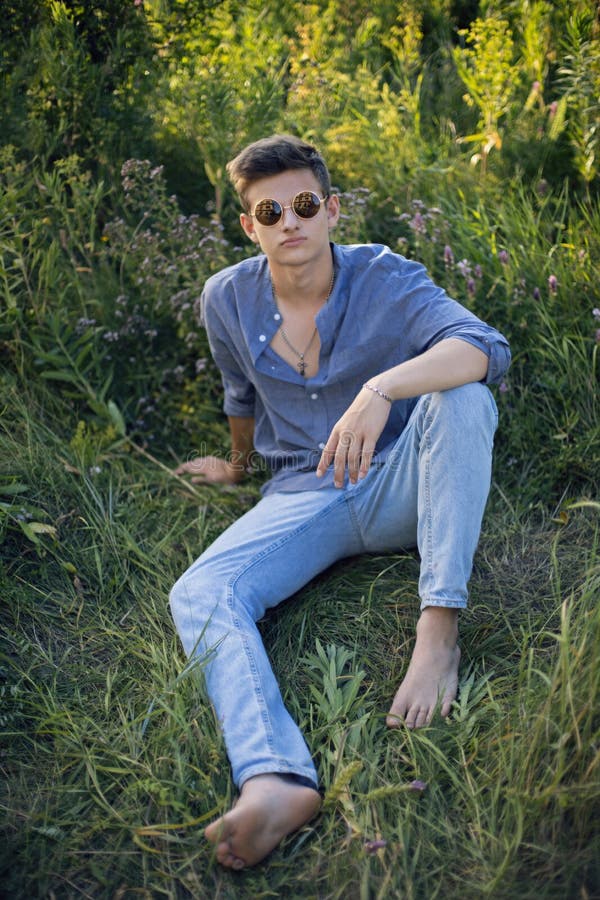 Teen Guy in Sunglasses is Sitting on the Grass in Nature in a Shirt and  Jeans Stock Image - Image of grass, handsome: 231383091