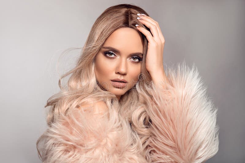 Sexy woman wears in pink fur coat. Ombre blond hairstyle. Beauty fashion blonde portrait. Beautiful girl model with makeup, long healthy hair style posing isolated on studio grey background