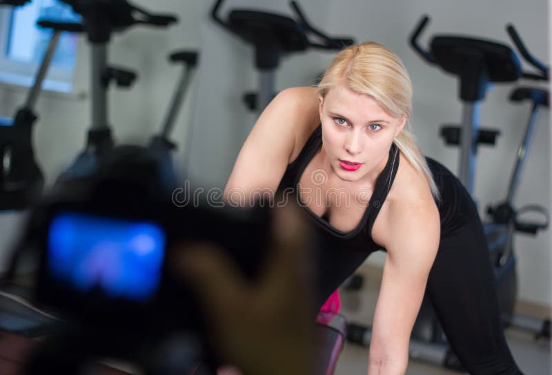 young athletics girl doing dumbbells press exercises. Fitness muscled woman in black sport clothing workout on bench in gym