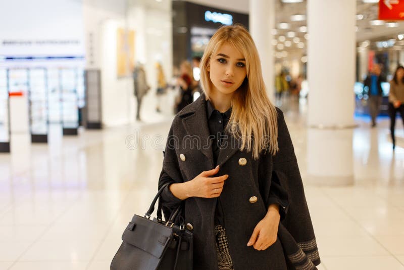 Sexy young blond woman model in a chic fashionable coat with a fashionable leather black fashion handbag