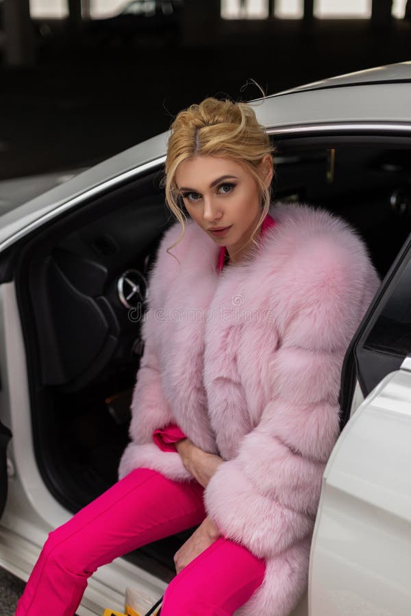 Sexy young fashion model beautiful woman in luxurious pink fur coat in glamorous fashionable pants with stylish hairstyle posing