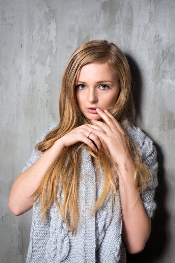 Young Longhair Blonde Woman In Knitted Sweater Posing Against Grungy