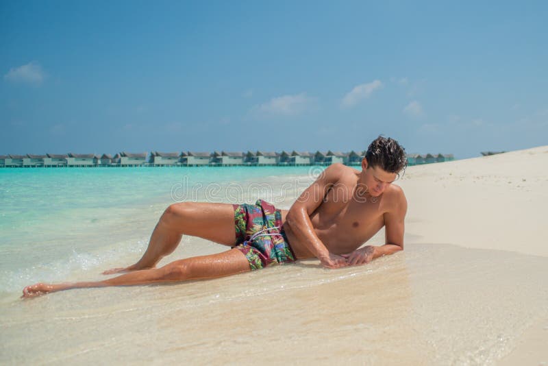 Sexy young male model relaxing at the beach at the tropical island luxury resort in Maldives