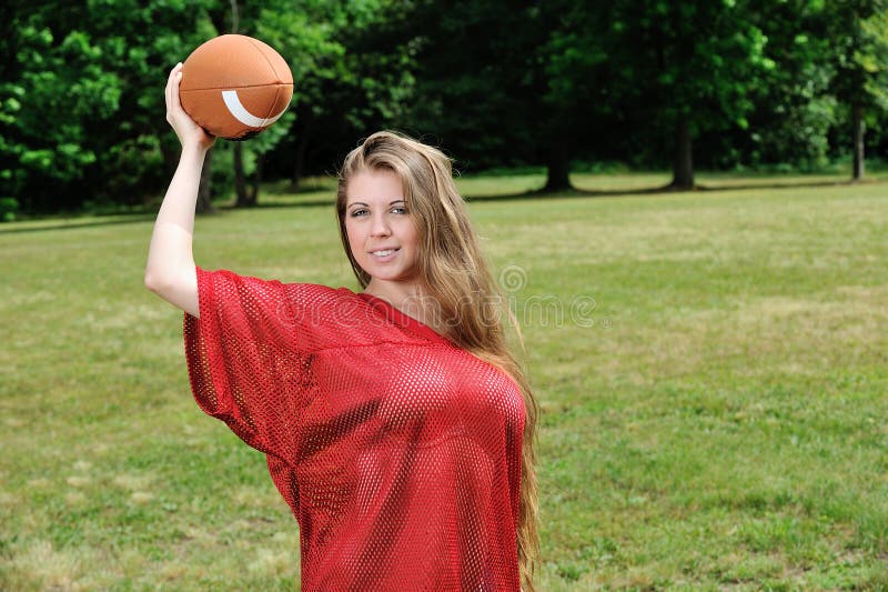 young Caucasian woman in red football jersey prepares to throw an American football. young Caucasian woman in red football jersey prepares to throw an American football