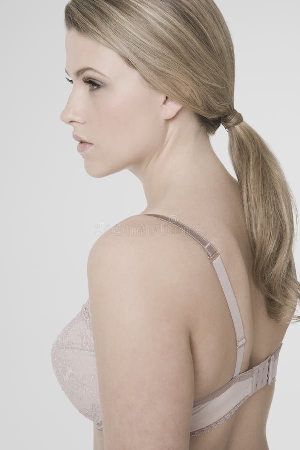 Closeup side view of a young woman in bra against gray background.