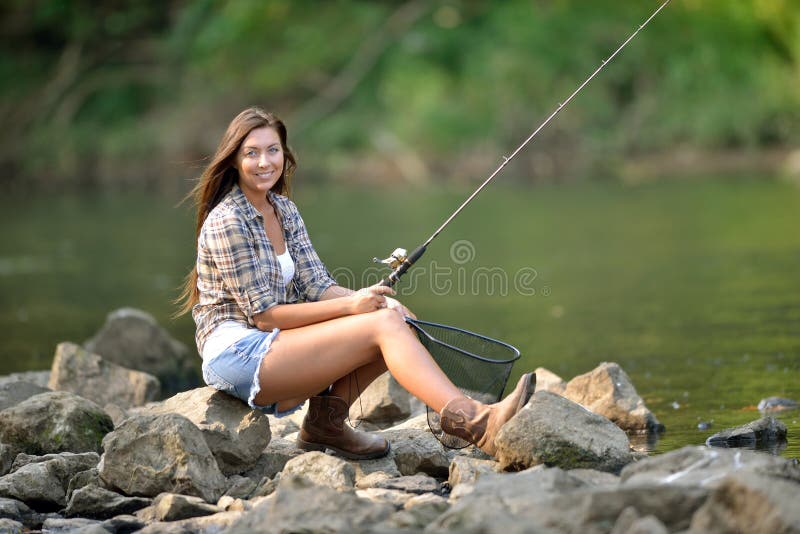 Sexy young woman sitting near river fishing