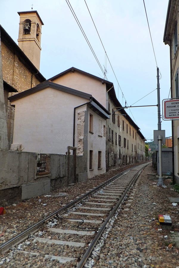 Seção de uma estrada de ferro single-track em Como, Itália, correndo em um espaço estreito entre casas, com uma torre de sino da imagem de stock Seção de uma estrada de ferro single-track em Como, Itália, correndo em um espaço estreito entre casas, com uma torre de sino da imagem de stock