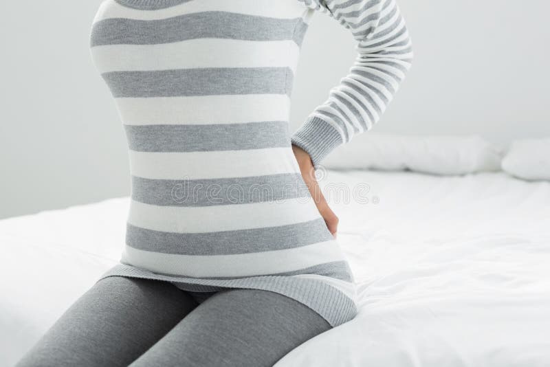 Seção meados de uma mulher com a dor traseira que senta-se na cama fotos de stock Seção meados de uma mulher com a dor traseira que senta-se na cama fotos de stock