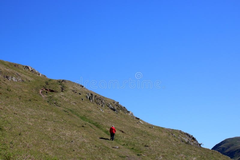 Señora en chaqueta roja que camina, trayectoria de la ladera, Cumbria imagen de archivo libre de regalías Señora en chaqueta roja que camina, trayectoria de la ladera, Cumbria imagen de archivo libre de regalías