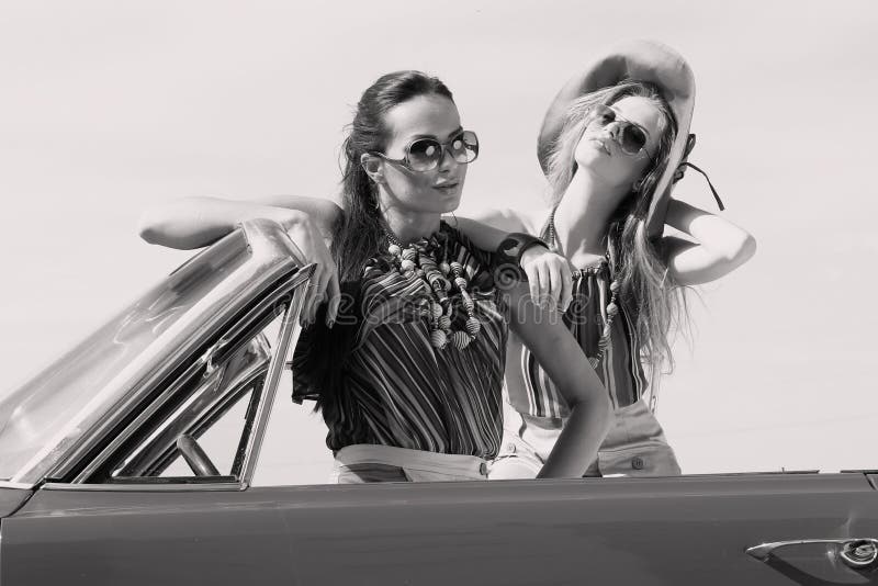 Señoras hermosas con los vidrios de sol que presentan en un coche del vintage en un verano de la primavera del día soleado imágenes de archivo libres de regalías Señoras hermosas con los vidrios de sol que presentan en un coche del vintage en un verano de la primavera del día soleado imágenes de archivo libres de regalías