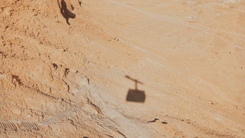 Shadow of a ropeway cabin rising in Masada desert. Aerial cable car going up on a sunny day. Sand and rocks. Israel 4K.