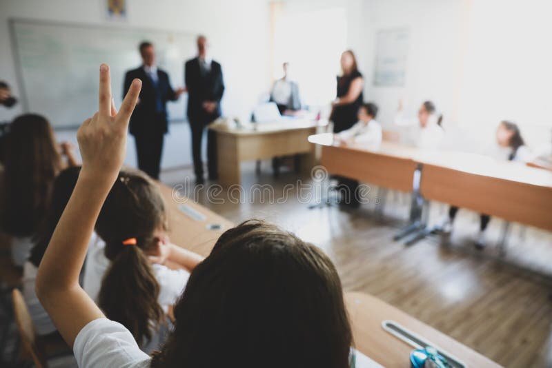 Shallow depth of field image with a pupil raised hand to answer or put a question or to volunteer for a task in the classroom royalty free stock image