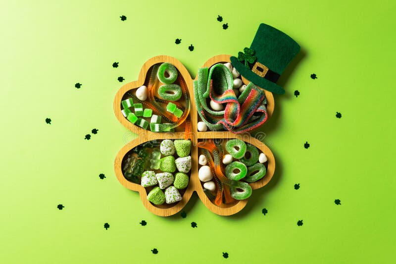 Shamrock-bricka fylld med gröna candies och sötsaker och med en liten leprechaun-hatt på en ljusgrön bakgrund med spridd royaltyfri fotografi