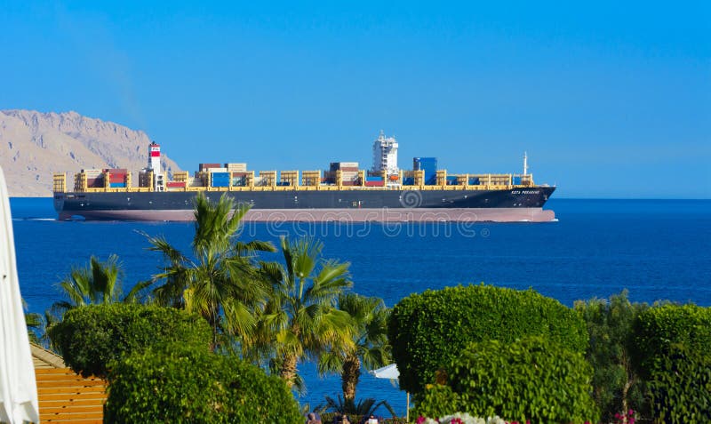 Sharm el-Sheikh, Egypte - Maart 14, 2018 Een reusachtig vrachtschip draagt containers met lading in het Rode Overzees tegen de bl royalty-vrije stock afbeelding Sharm el-Sheikh, Egypte - Maart 14, 2018 Een reusachtig vrachtschip draagt containers met lading in het Rode Overzees tegen de bl royalty-vrije stock afbeelding