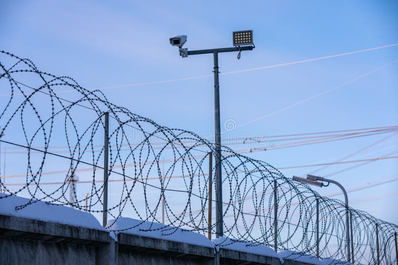 Sharp pointed razor wire barbed fence coiled on top of wall protects from prisoners and criminals in prison and from