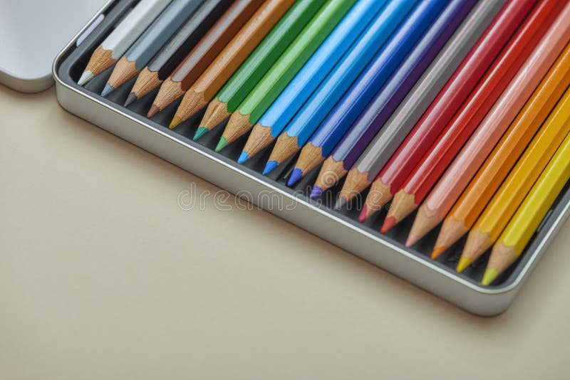 Sharpened colored pencils aligned diagonally inside metal case on neutral background