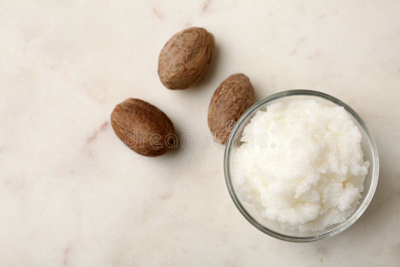 Shea butter in bowl and nuts on table, top view. stock photography