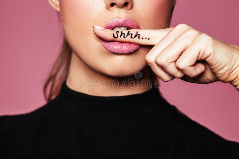 Shh! Women`s secrets. Cropped shot of female with finger in mouth. Closeup portrait of young woman is showing a sign of silence with shhh written on the finger. Shh! Women`s secrets. Cropped shot of female with finger in mouth. Closeup portrait of young woman is showing a sign of silence with shhh written on the finger.