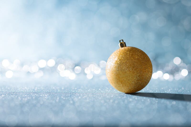 Shiny Gold Christmas Bauble in Winter Wonderland. Blue Christmas background with defocused christmas lights.