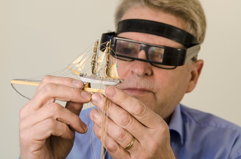 Ship in a bottle builder. Examining and adjusting the rigging. Building bottle ship is a tradition among seamen dating back to the 19th century Ship in a bottle builder. Examining and adjusting the rigging. Building bottle ship is a tradition among seamen dating back to the 19th century