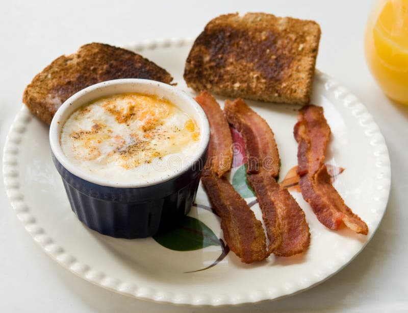 Shirred eggs (baked eggs with cheese and cream) in a ramekin, with toast and bacon. Shirred eggs (baked eggs with cheese and cream) in a ramekin, with toast and bacon