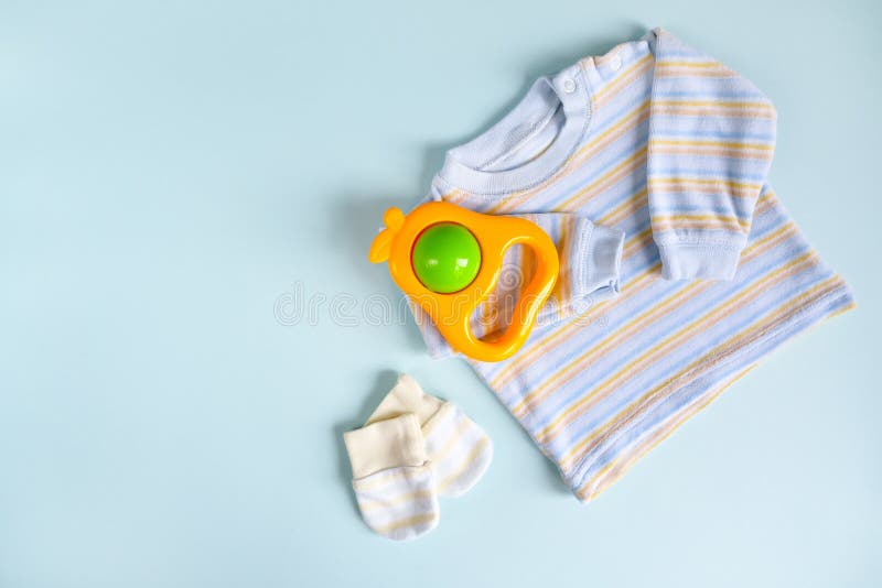 Shirt, mittens and rattle for newborn baby. Copy space. Infant clothes on blue background. Baby goods. stock images