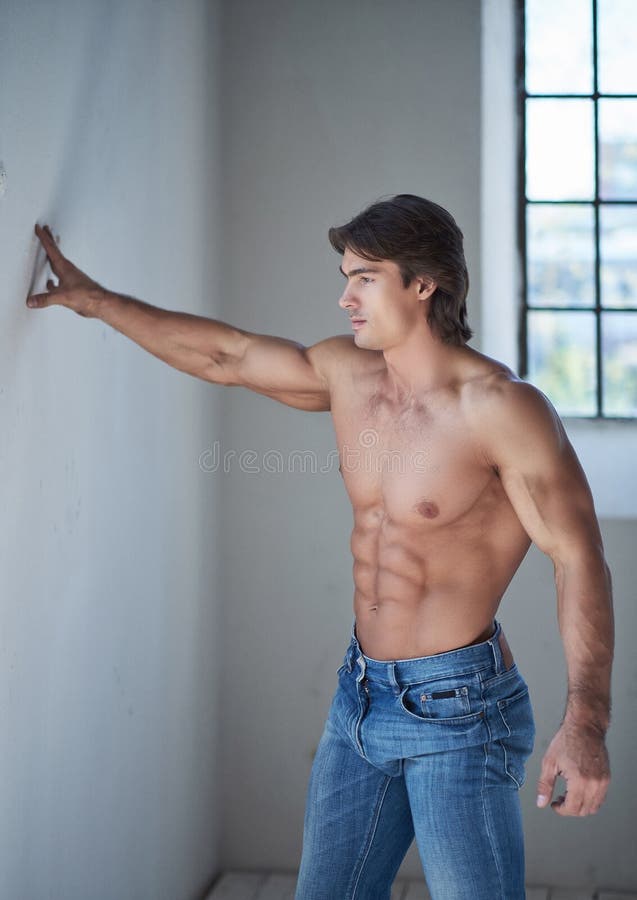 Shirtless knap mannetje met een perfect spierlichaam die op een muur in de studio leunen, die een venster bekijken stock afbeeldingen Shirtless knap mannetje met een perfect spierlichaam die op een muur in de studio leunen, die een venster bekijken stock afbeeldingen