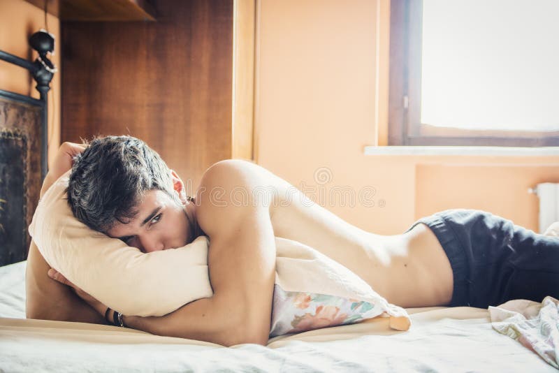 Shirtless sexig manlig modell som bara ligger på hans säng arkivbild Shirtless sexig manlig modell som bara ligger på hans säng arkivbild