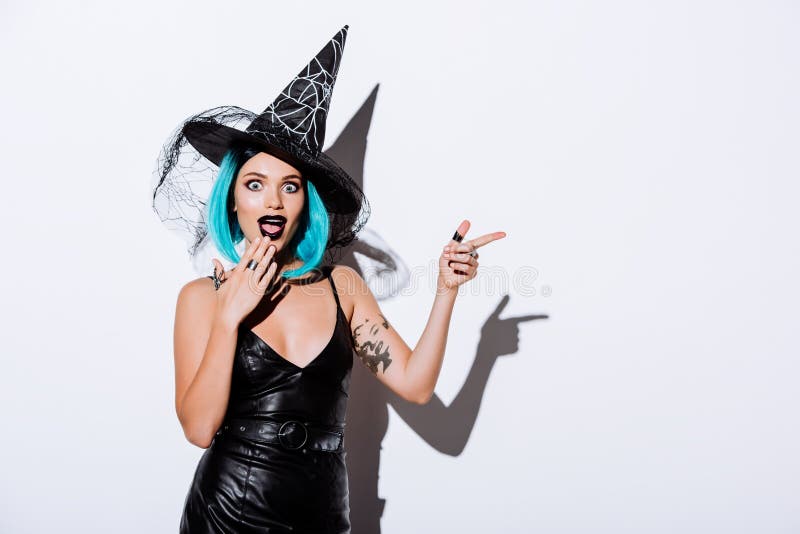Shocked girl in black witch Halloween costume with blue hair pointing with finger