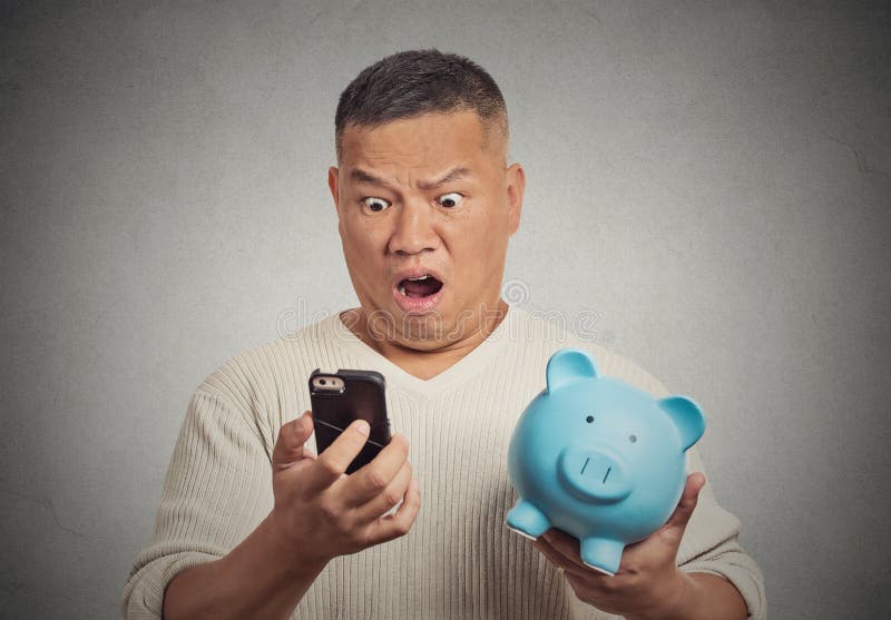 Shocked man looking at his smart phone holding piggy bank royalty free stock images Shocked man looking at his smart phone holding piggy bank royalty free stock images
